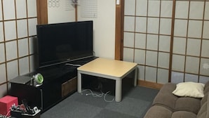 A compact living space with a television, a small table, a sofa, and a futon. - Hikawacho Guest House (Soka)