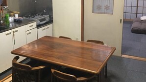 A compact kitchen with a gas stove, white cabinets, and a wooden dining table with four chairs. - Hikawacho Guest House (Soka)