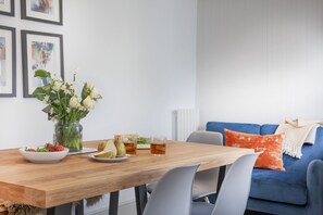 Un coin repas avec une table en bois, des chaises, un vase de fleurs, un saladier et une assiette de fruits.