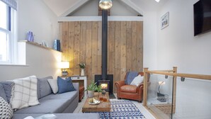 A cozy living room with a sofa, a coffee table, a fireplace, and a glass railing. - Birdcage Cottage- Woodburner & Free Wi-Fi (Kingsand)