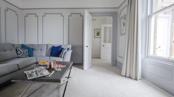 A living room with a grey sofa, a coffee table, and a door leading to another room.