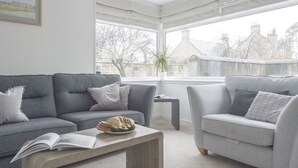 A living room with two grey sofas, a coffee table, and a window with a view of buildings and trees. - Whitecraigs -  a rural that sleeps 8 guests  in 4 bedrooms (Elgin)