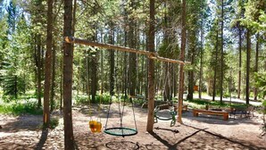 A forested area with a swing set, a bench, and a picnic table. - Moose Tracks Inn: Family Friendly and Wheelchair Accessible. (Island Park)