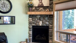 A stone fireplace with a mounted clock and a deer painting above it. - Moose Tracks Inn: Family Friendly and Wheelchair Accessible. (Island Park)
