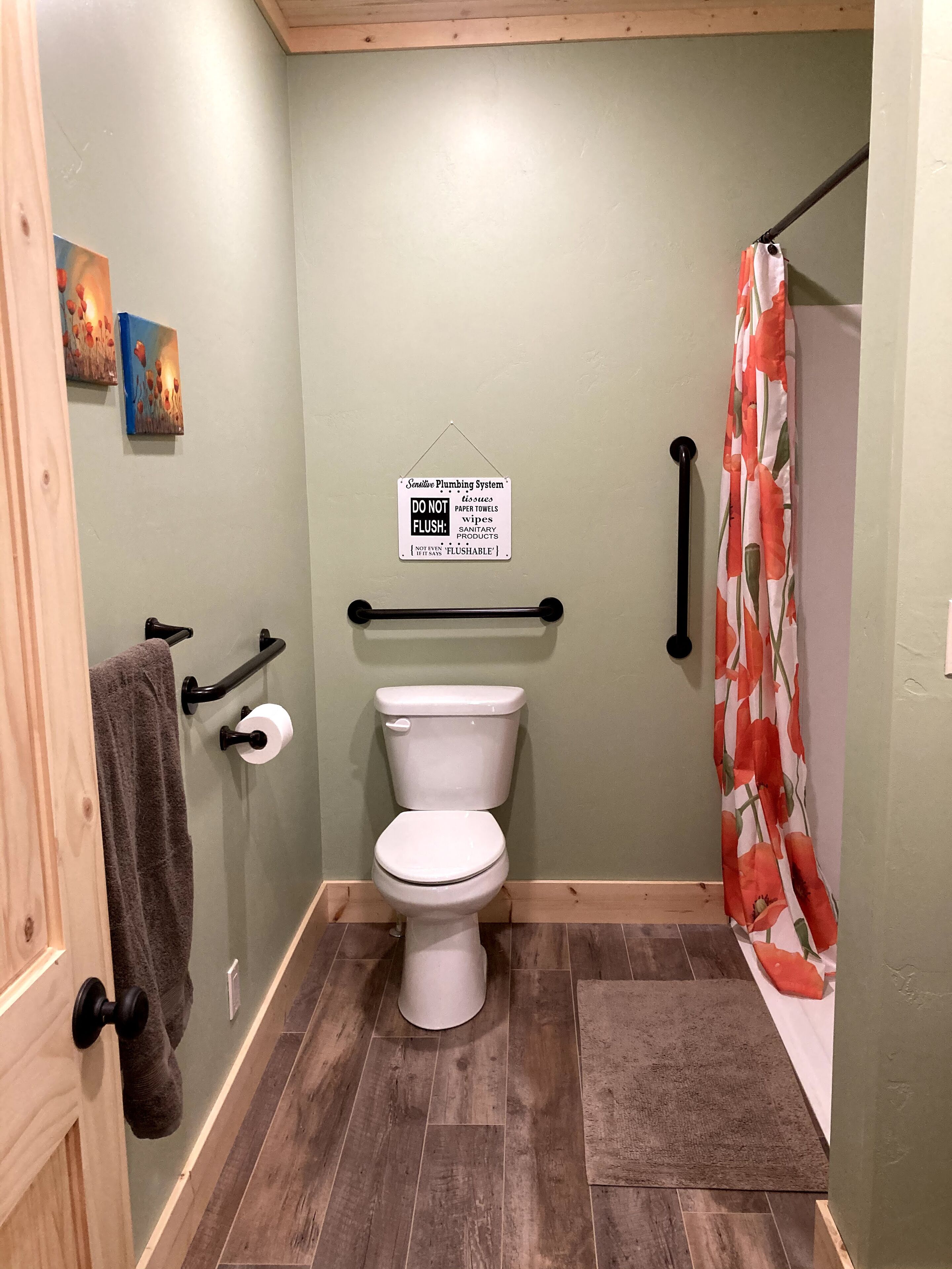 Un baño pequeño y privado con inodoro, barandilla, cortina de ducha y un cartel que prohíbe arrojar objetos no aptos para el desagüe.