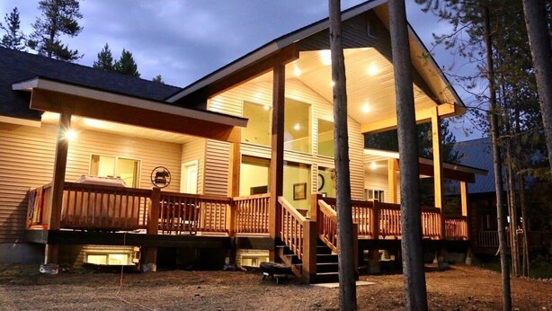 A two-story house with a wooden deck, a covered porch, and a staircase leading to the upper floor. - Moose Tracks Inn: Family Friendly and Wheelchair Accessible. (Island Park)