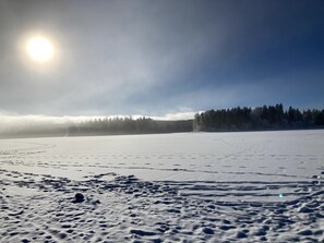 Ett snötäckt landskap med en klar himmel och en skog i bakgrunden.