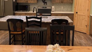 A kitchen with wooden cabinets, a refrigerator, a microwave, an oven, and a dining area with chairs and a table. - Moose Tracks Inn: Family Friendly and Wheelchair Accessible. (Island Park)
