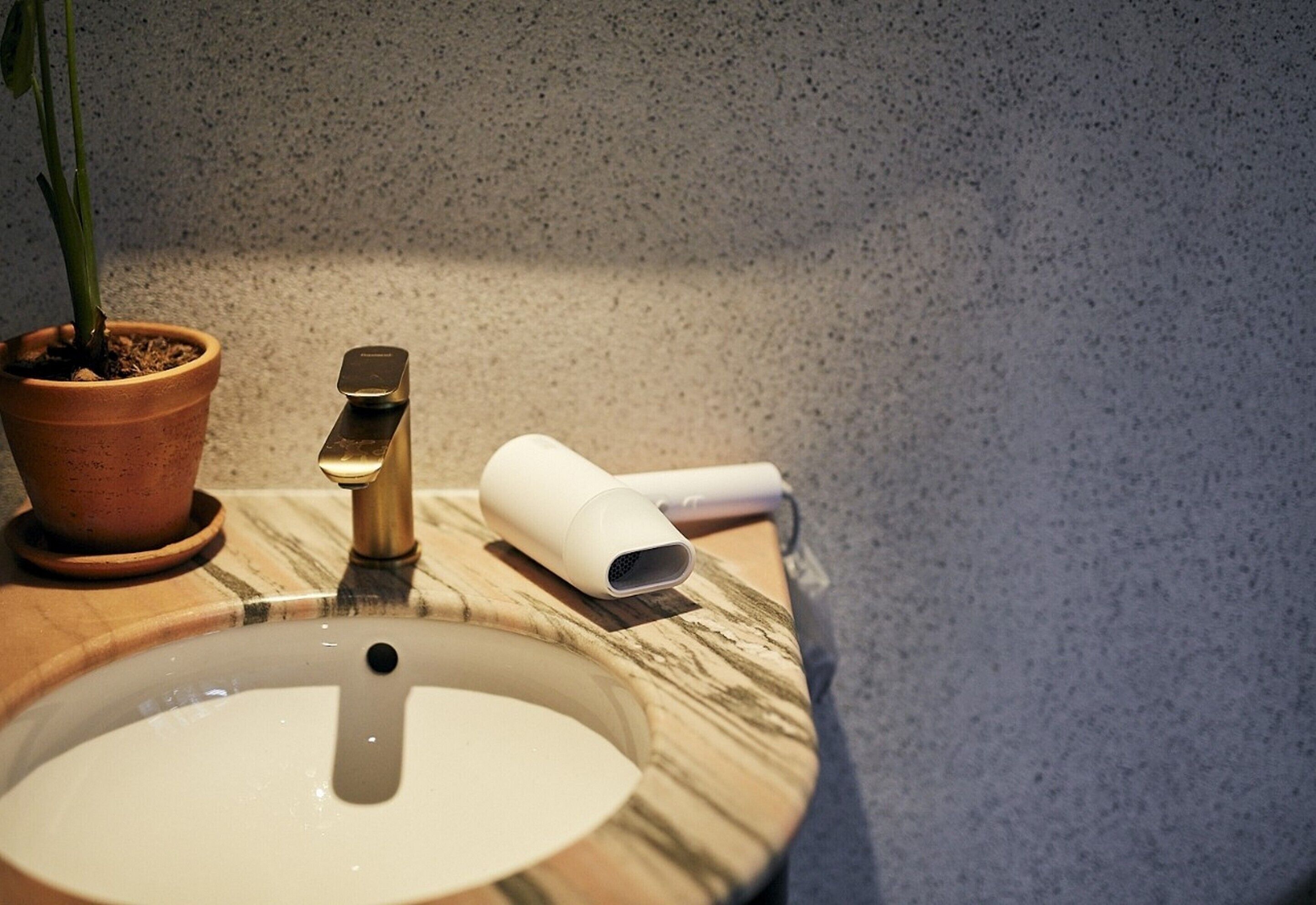 A bathroom sink with a marble countertop, a potted plant, and a handheld device on the counter.