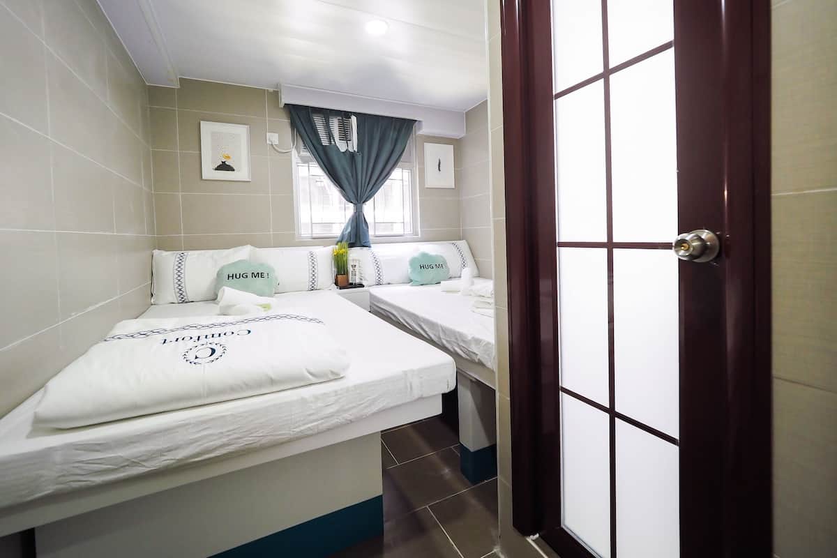 Quarto de hotel com duas camas, uma janela com cortinas, uma porta e um ar condicionado fixado na parede.