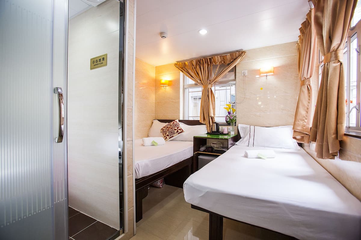 Quarto de hotel com duas camas, uma mesinha, uma mesa de cabeceira, uma janela com cortinas e um aviso indicando o andar.
