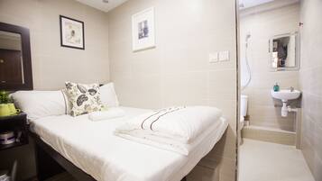 A hotel room with a bed, a bedside table with a plant, a bathroom with a shower and sink.