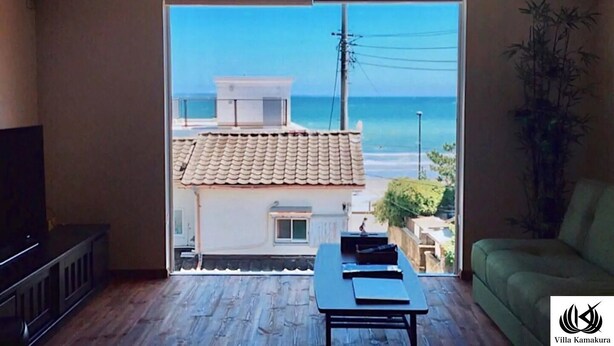 Sala de estar com vista para a praia, televisão, uma mesa com objetos e um sofá.