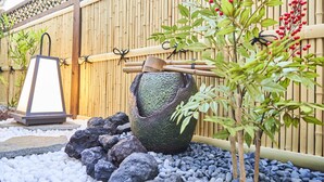 Um jardim com um candeeiro de pedra, cerca de bambu e uma árvore bonsai.
