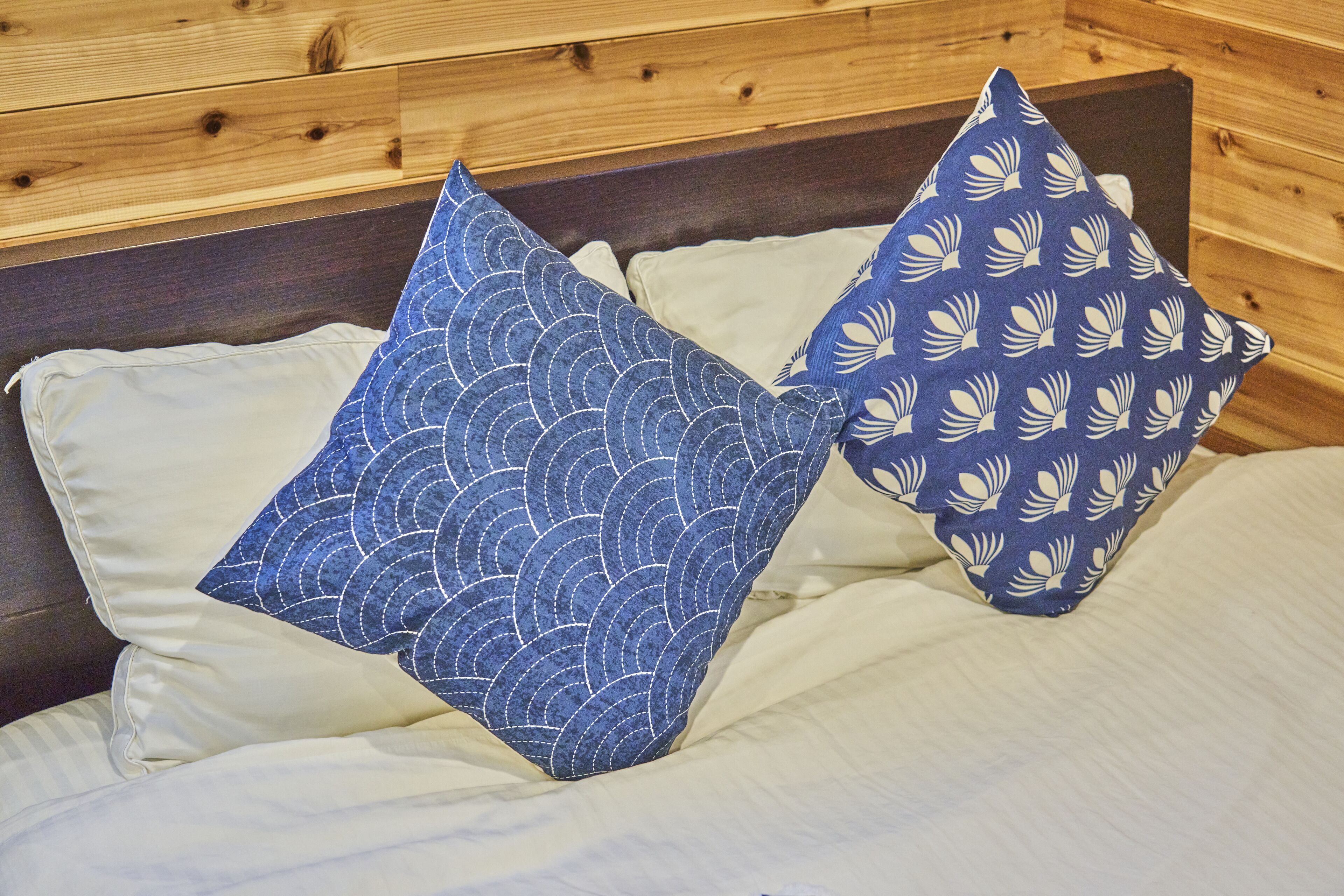 A bed with two pillows, one with a blue wave pattern and the other with a white shell pattern, against a wooden headboard.