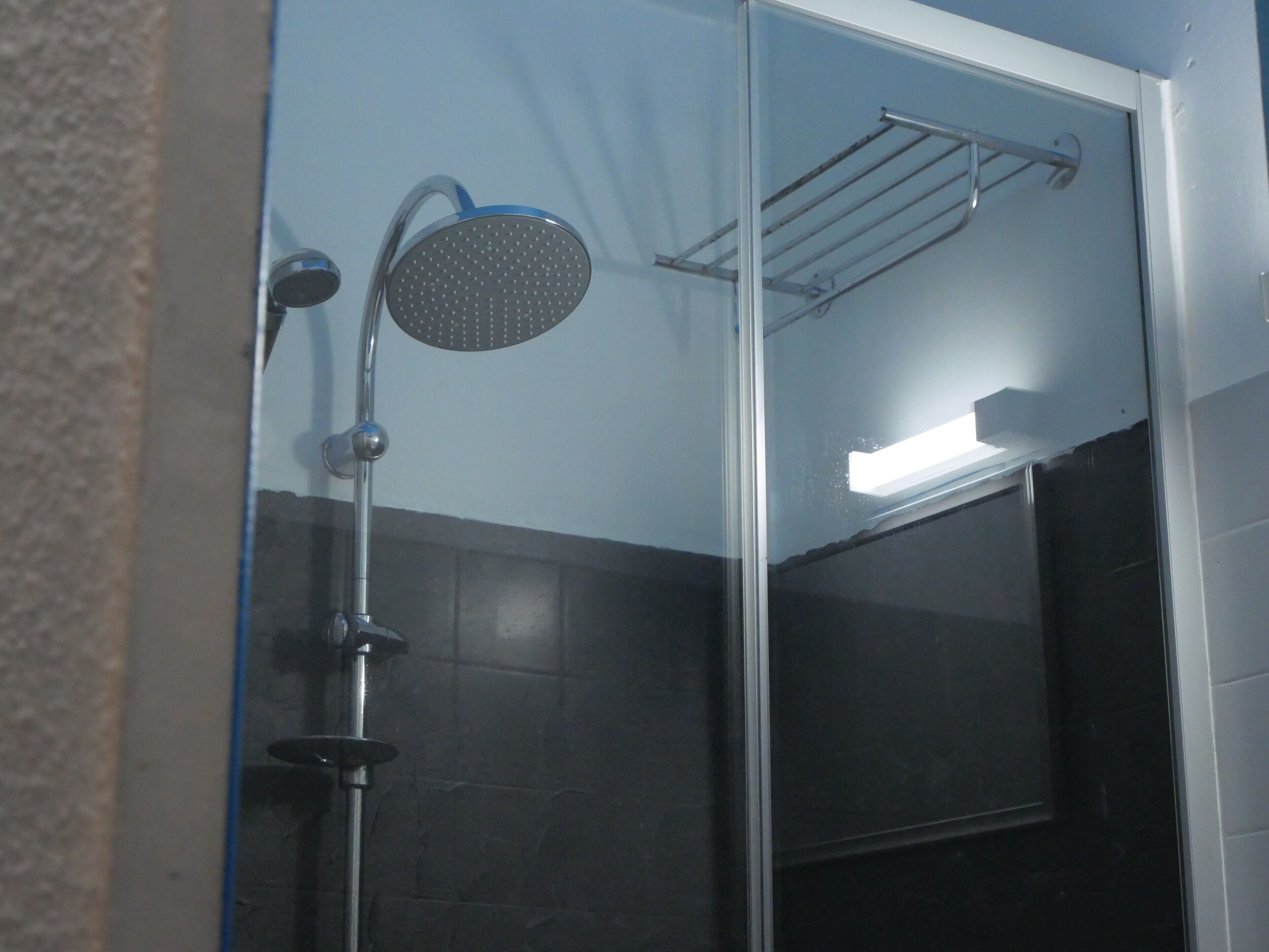 A glass-enclosed shower with a handheld showerhead and a wall-mounted faucet.