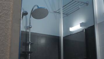 A glass-enclosed shower with a handheld showerhead and a wall-mounted faucet.