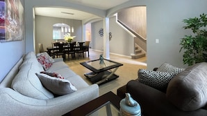 A spacious living room with a grey sofa, a brown sofa, and a coffee table. There is a dining area with a table and chairs, and a staircase leading to another level. - Serenity By Your Private Pool! Excellent Reviews! Resort Living! 4396 (Davenport)