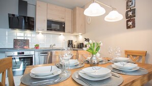 Een moderne keuken met houten kasten, roestvrijstalen apparatuur en een eettafel gedekt voor zes personen, met borden, glazen en bestek.