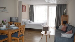 Een moderne hotelkamer met een bed, een bank, een eettafel met stoelen, een televisie en een bureau met een lamp.
