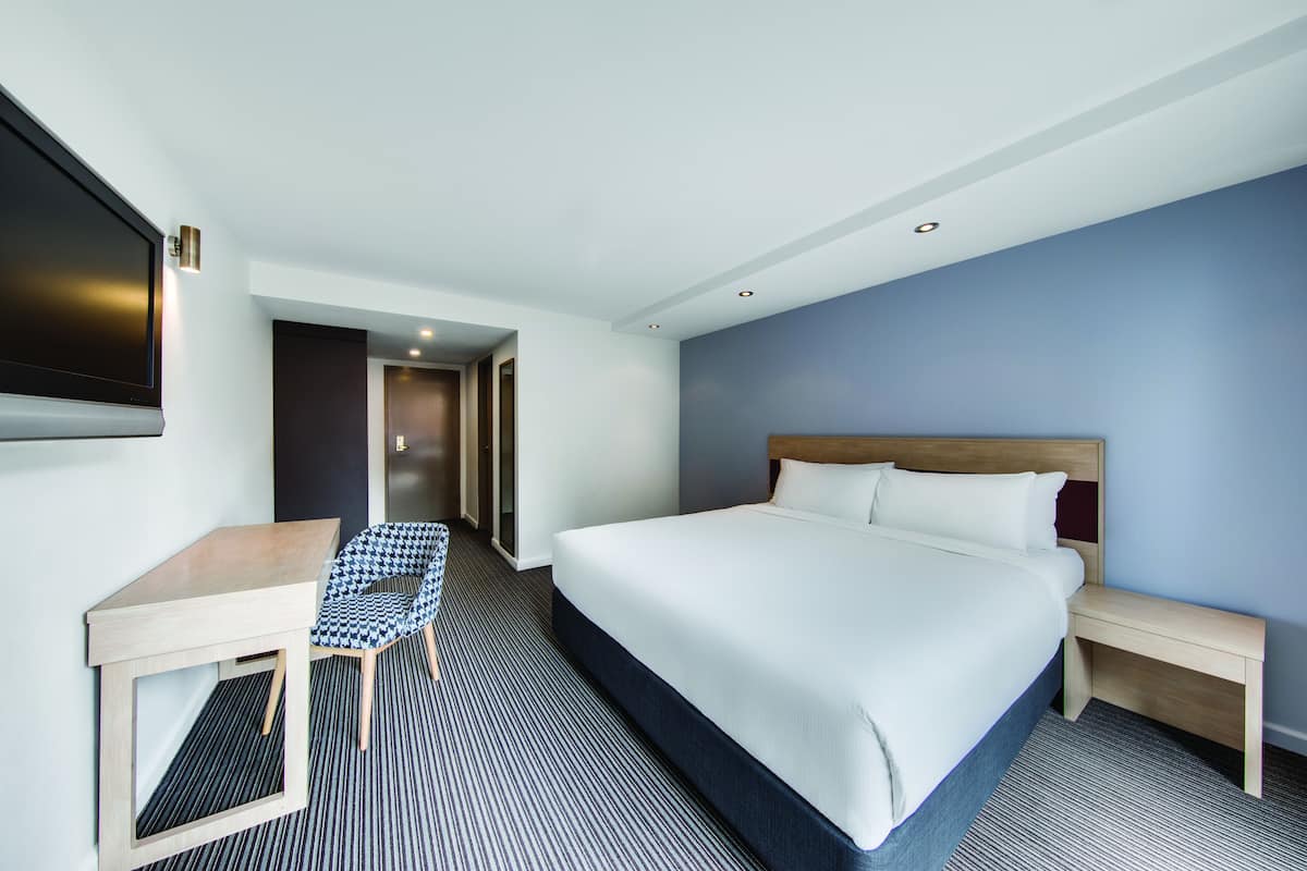 Habitación de hotel con una cama grande, un escritorio, una silla y un televisor.