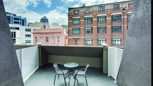 A balcony with a table and chairs, overlooking a cityscape with various buildings, including a pink building labeled "Crystal Palace Hotel". - Central Studio Hotel Sydney (Haymarket)