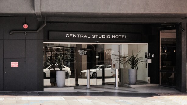The entrance to Central Studio Hotel with a glass facade, a white car parked outside, and a potted plant near the entrance. - Central Studio Hotel Sydney (Haymarket)