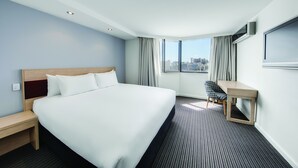A hotel room with a large bed, a desk, a chair, and a view of the city through the window. - Central Studio Hotel Sydney (Haymarket)