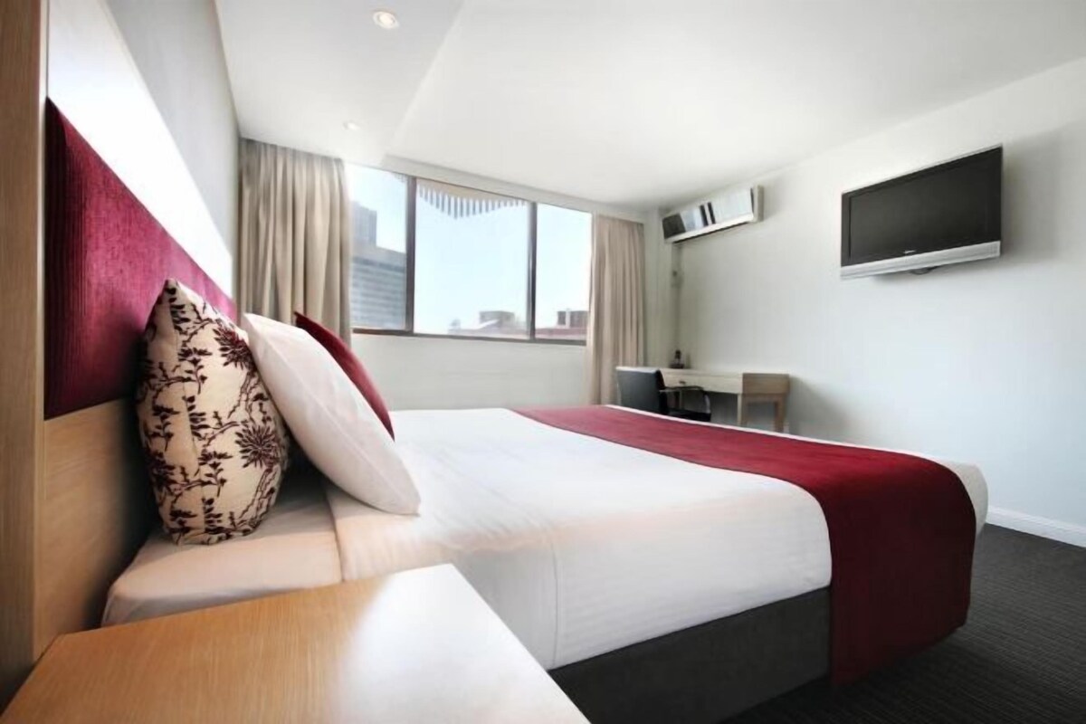 Een hotelkamer met een bed, een bureau, een stoel, een televisie en een raam met gordijnen.