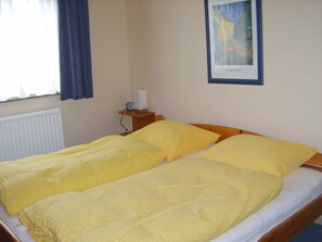 Una cama doble con ropa de cama amarilla, una mesita de noche con lámpara y un cuadro en la pared.