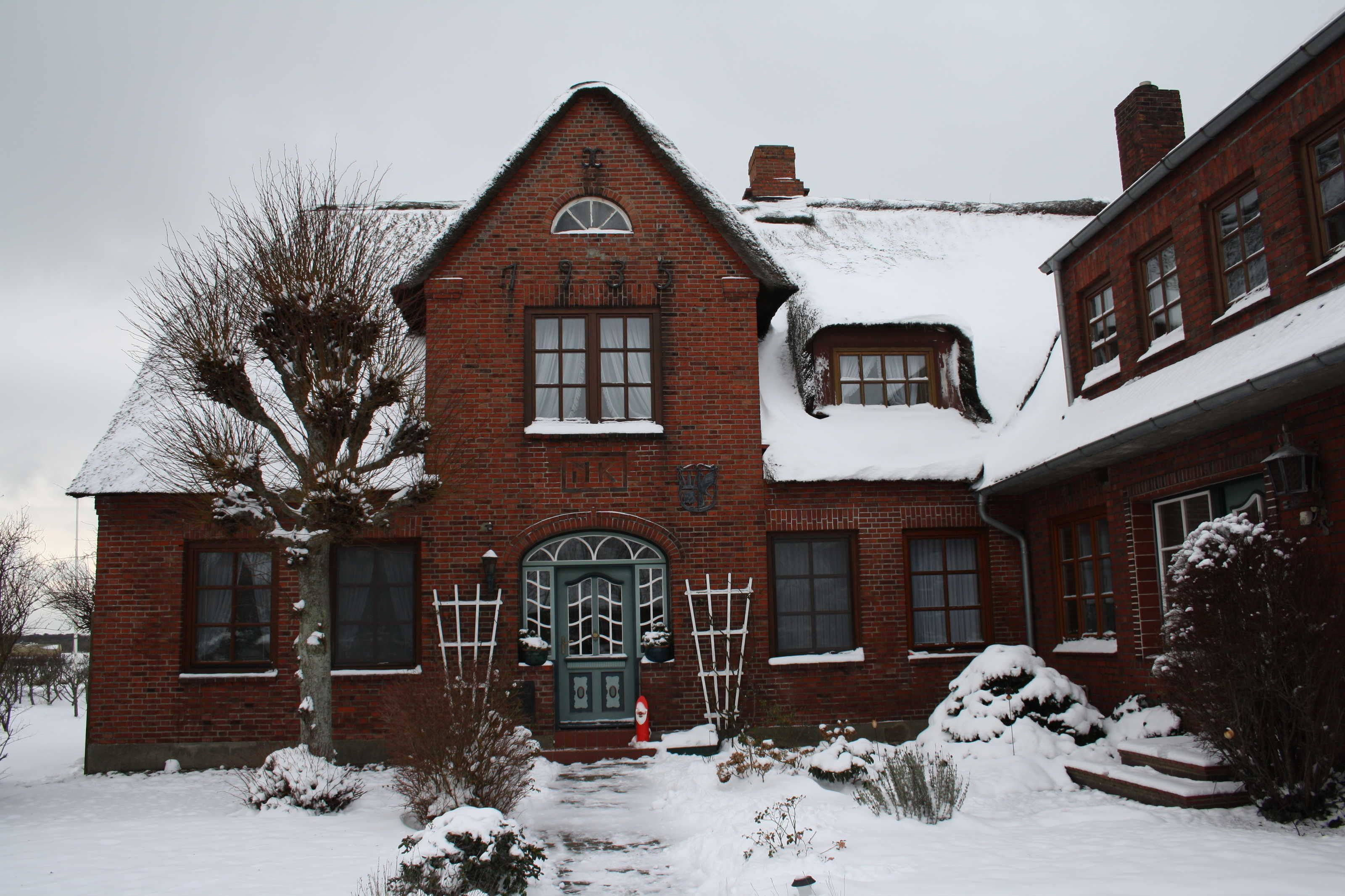 A red brick house with a snow-covered roof and a green door.
