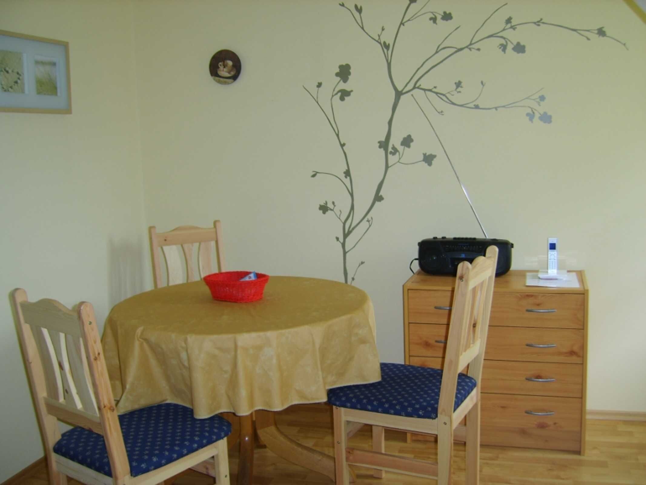 Un comedor con una mesa, sillas, un tazón rojo, una radio y un mueble pequeño.