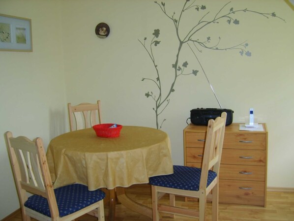 A dining area with a table, chairs, a red bowl, a radio, and a small cabinet.