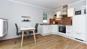 Een moderne keuken met witte kasten, een houten aanrecht en een eethoek met een tafel en stoelen.