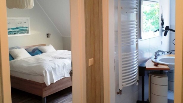 Ein Schlafzimmer mit Bett, Heizkörper und einem Badezimmer mit Waschbecken und Spiegel.