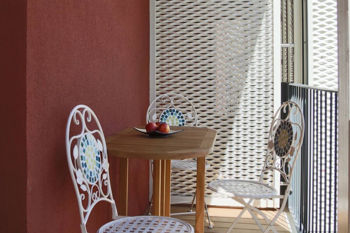 A wooden deck with a table and two chairs, a white mesh partition, and a metal railing.