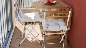 Una terraza de madera con una mesa y sillas, una mesita con manzanas y una pared roja.