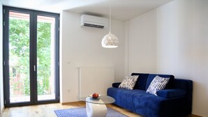 Una sala de estar moderna con un sofá azul, cojines estampados, una mesa de centro de vidrio y una lámpara colgante de diseño geométrico.