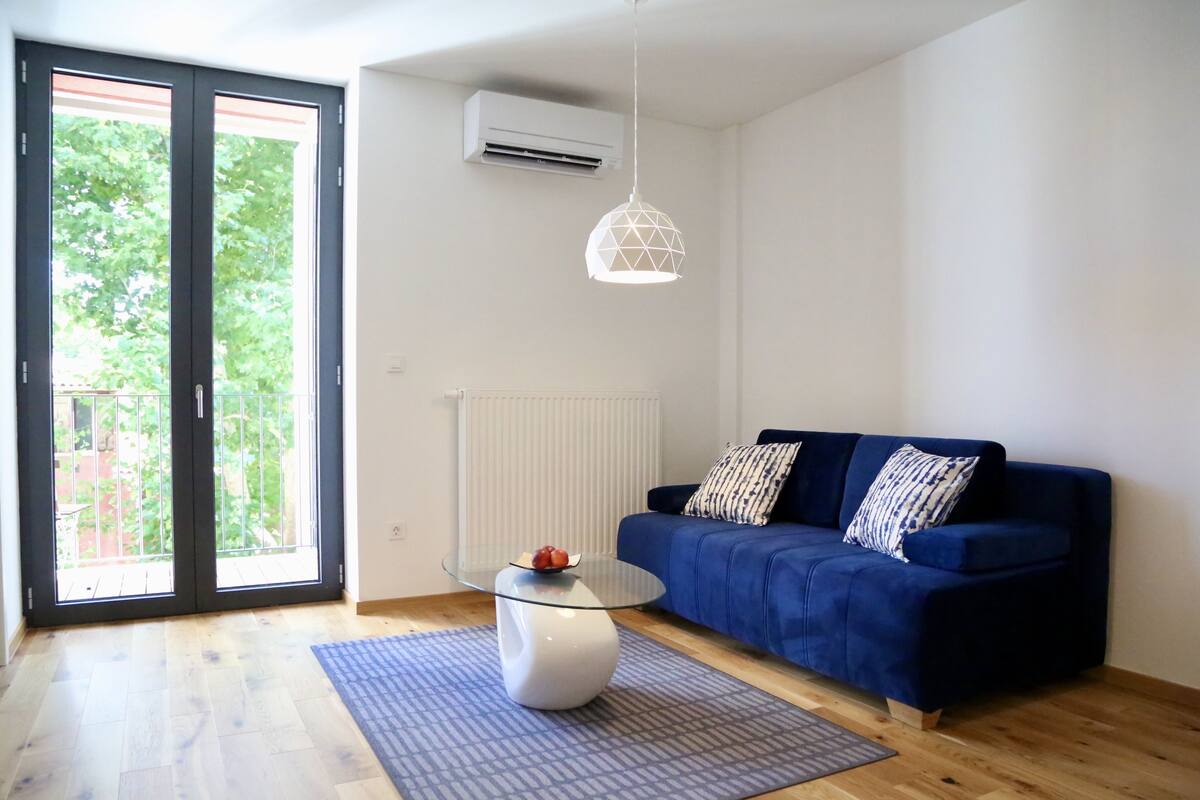A modern living room with a blue sofa, patterned cushions, a glass coffee table, and a geometric pendant light.