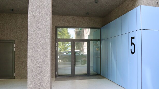 Una entrada de edificio con puerta de vidrio, pared azul con el número 5 y suelo de baldosas.