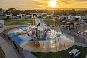 Un parc aquatique avec des toboggans et une piscine, entouré d’une clôture et agrémenté de tables de pique-nique.