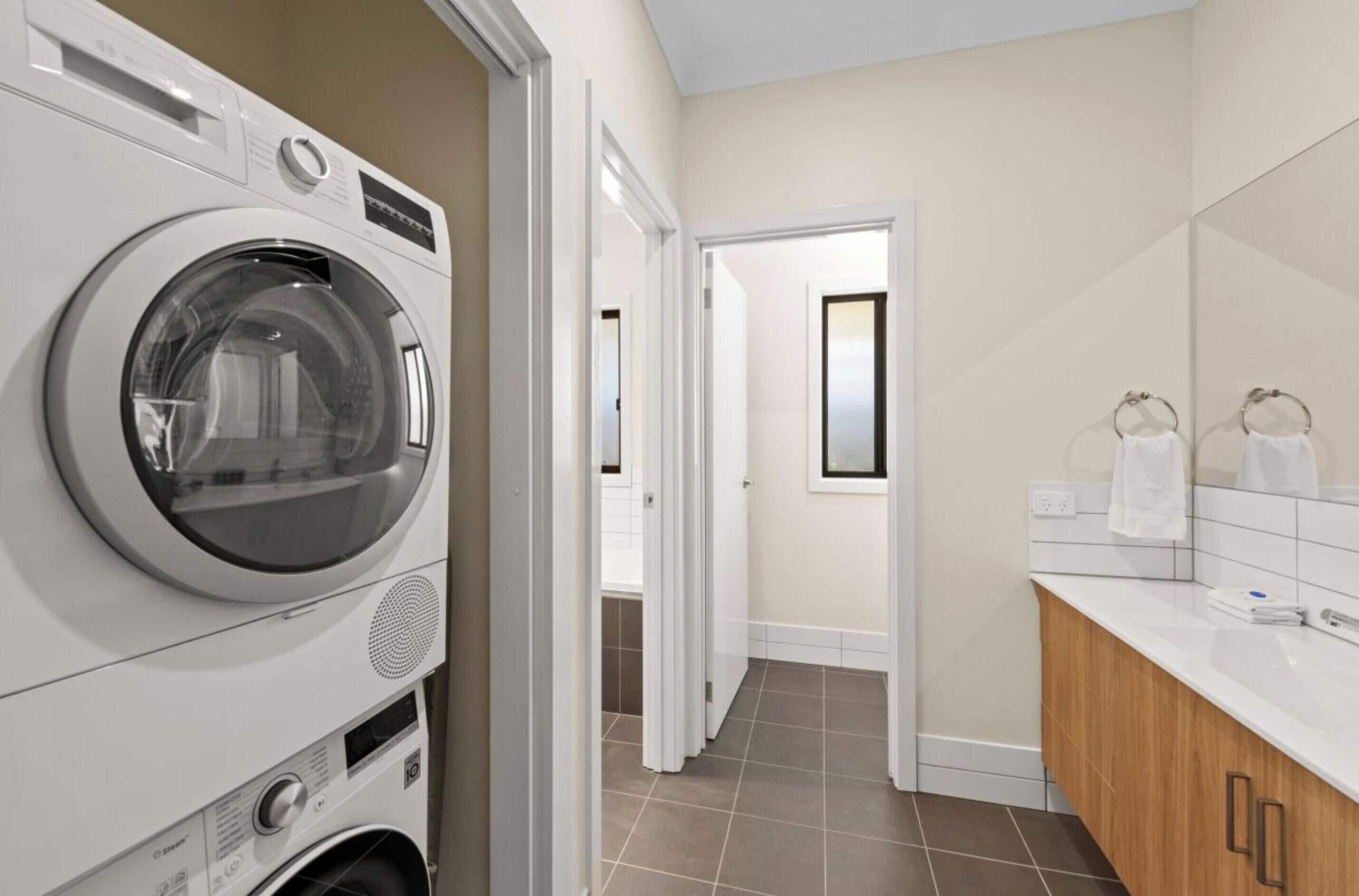 A laundry area with stacked washing machines, a wooden cabinet, and a tiled floor.