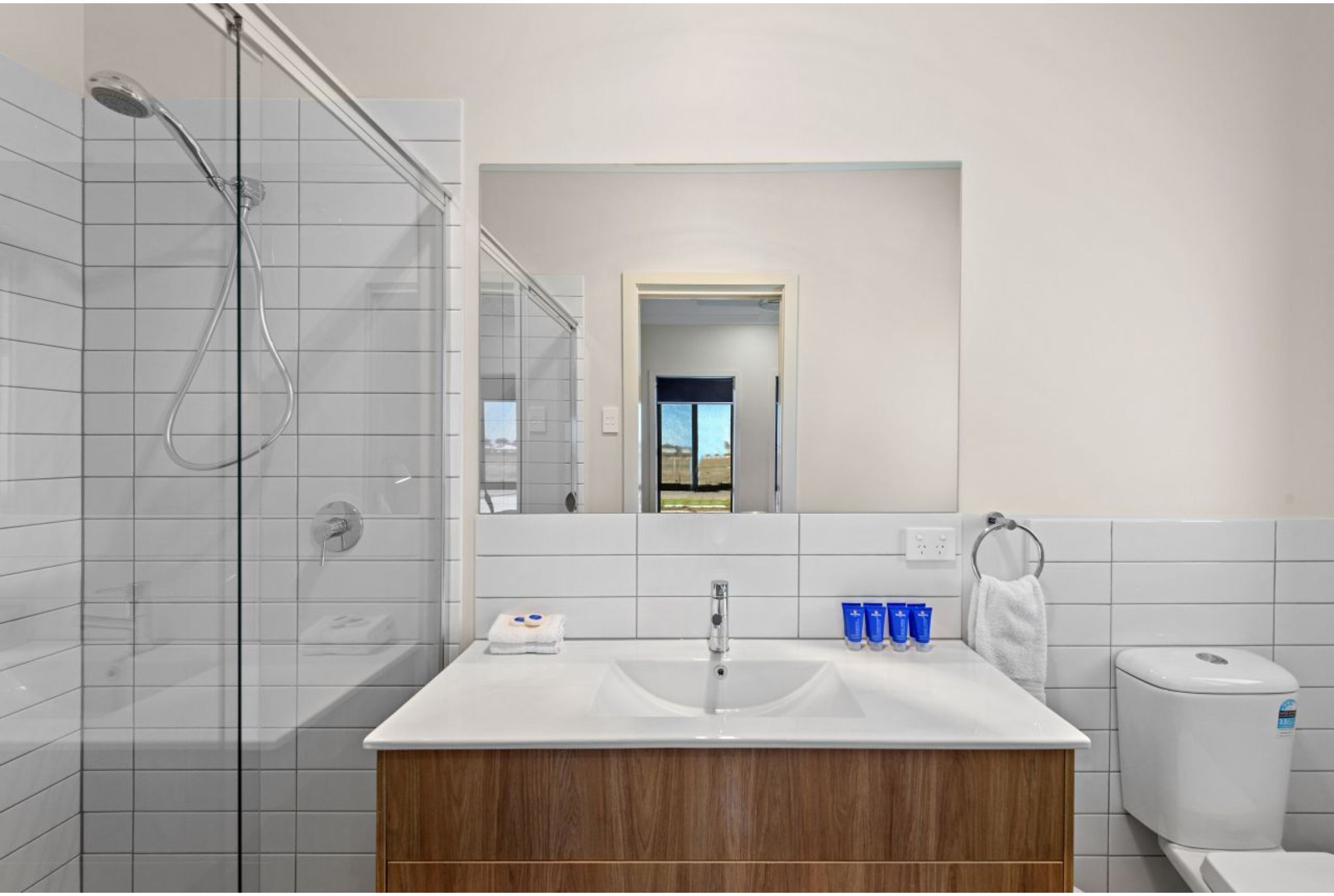 A modern bathroom with a glass shower enclosure, a white sink with a wooden vanity, and a toilet.