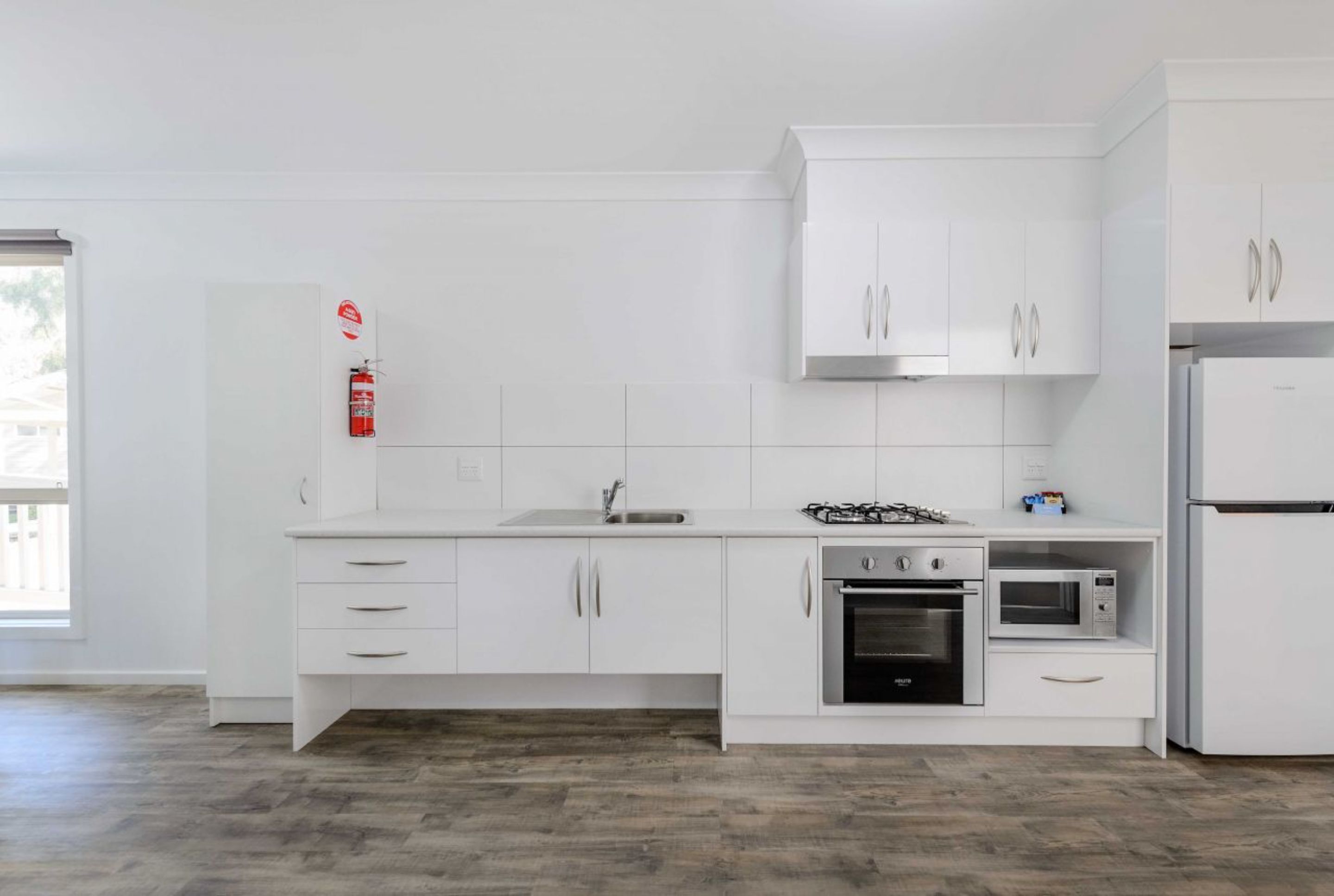 Une cuisine moderne avec des meubles blancs, une cuisinière à gaz, un four et un four à micro-ondes.