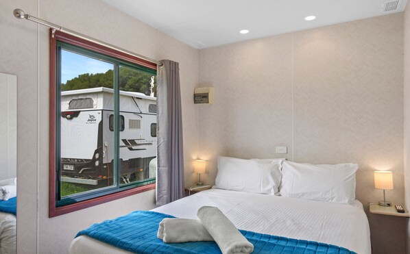 Habitación de hotel con un ventanal grande, una cama con ropa blanca, un plaid azul y dos lámparas de noche.