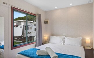 A hotel room with a large window, a bed with white linens, a blue throw blanket, and two bedside lamps.