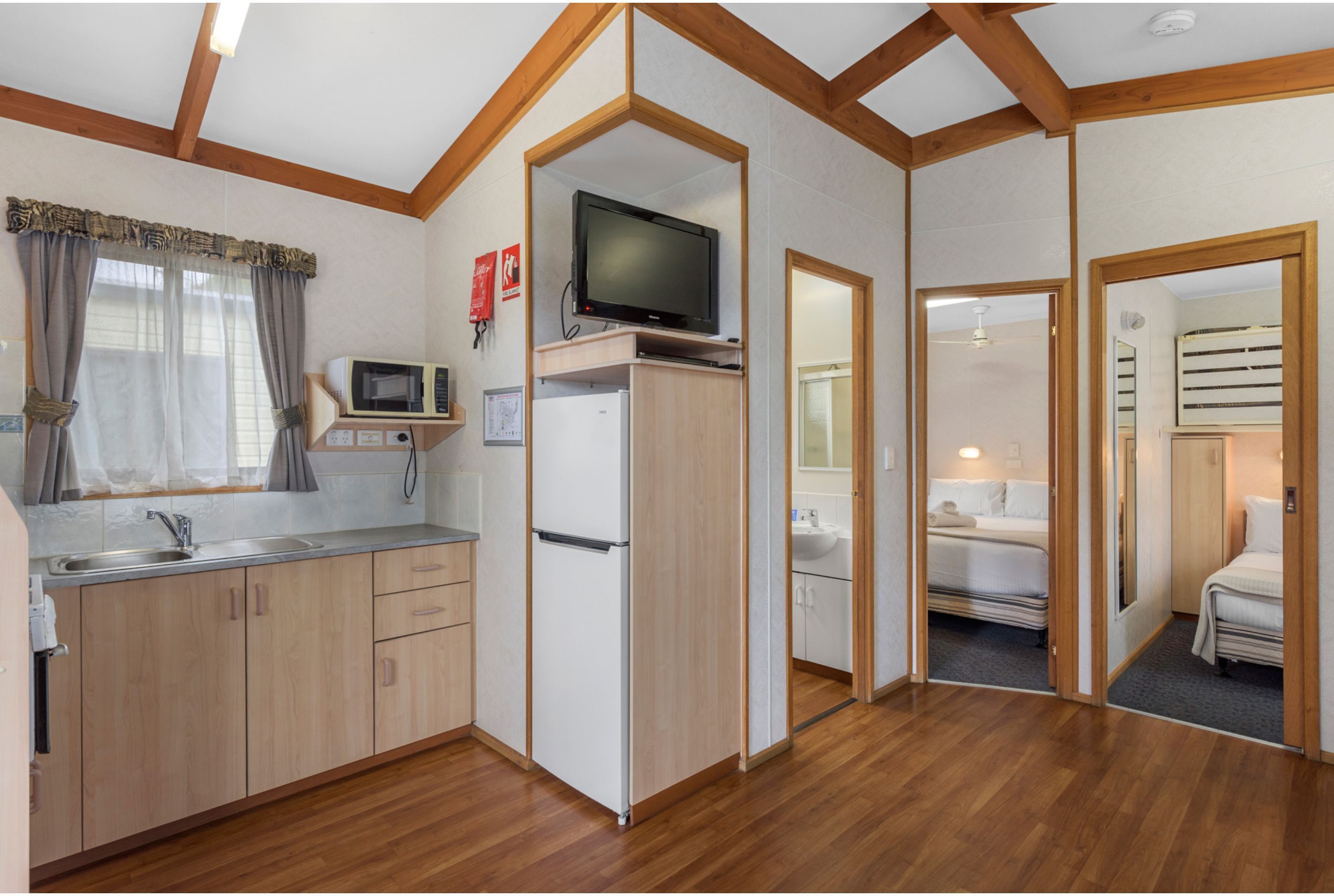 Una cocina compacta con microondas, refrigerador y televisor sobre una repisa de madera.