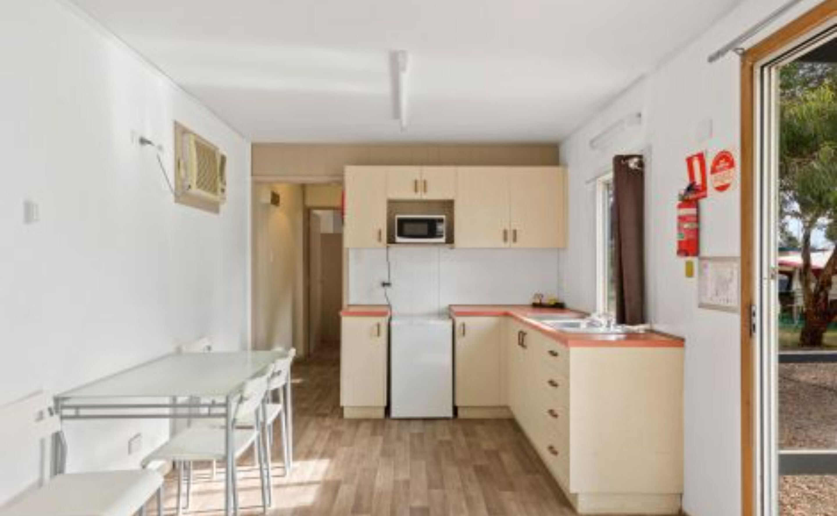 Een kleine keuken met een magnetron, een koelkast en een eethoek met een tafel en stoelen.