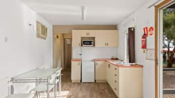 Een kleine keuken met een magnetron, een koelkast en een eethoek met een tafel en stoelen.