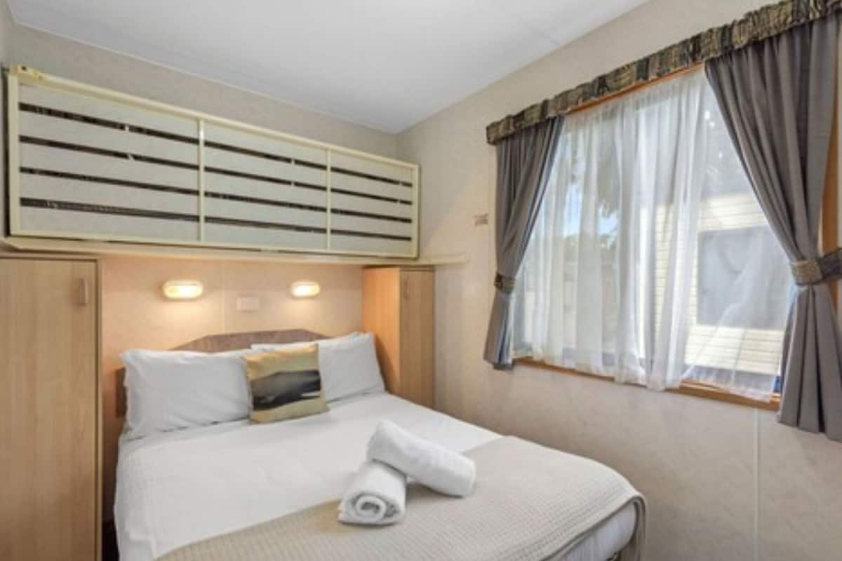 A hotel room with a bed, a window with curtains, a ceiling fan, and a wall-mounted air conditioning unit.